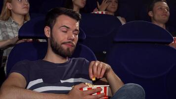 hermoso joven hombre masticando Palomitas, sensación aburrido durante un aburrido película video