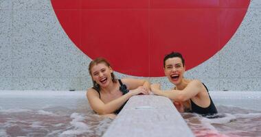 contento mujer disfrutando perezoso día en spa, dos bonito señoras amigos relajante en jacuzzi, sonriente video