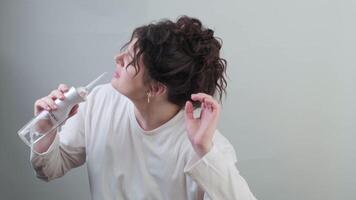 Smiling girl with hair in a bun uses a water flosser singing and dancing with joy spreading positive energy and morning vibes. video