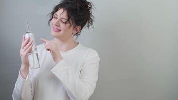 Woman in a white sweater holds a teeth irrigator, pressing the button to turn it on, showing how it works. video