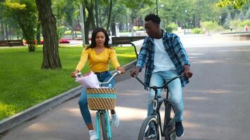 Two young friends ride bicycles together in a park, smiling and enjoying each other's company. The scene is vibrant with greenery and offers a sense of adventure and fun. video