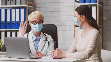 A nutritionist consults with a woman client in a bright and organized clinic. They discuss dietary options while maintaining health protocols with masks on and a laptop open for reference. video