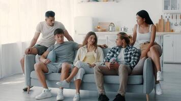 A group of diverse millennials sits together on a couch in a bright, inviting living room. They have intense conversation, creating a warm atmosphere of friendship and fun. video
