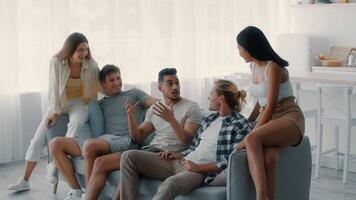 A group of diverse millennials share laughter and stories while relaxing together in a bright, stylish living room. The atmosphere is cheerful, highlighting friendship and connection. video
