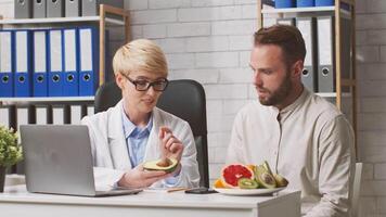 A healthcare professional discusses nutrition with a patient in a modern clinic. Fresh fruits are displayed on the table as they explore healthy dietary choices together. video