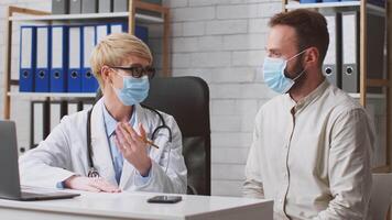 A healthcare professional in a lab coat discusses personalized nutrition strategies with a man patient. Both wear masks in a bright, organized clinic environment. video