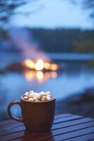 A mug of hot chocolate with marshmallows on a table in front of a fire photo