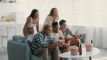 A group of five diverse friends is engaged in an exciting gaming session in a cozy living room. They are sharing laughter and snacks, demonstrating a relaxed and enjoyable atmosphere. video