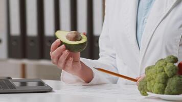 Dietitian at a clinic engages in a consultation focused on nutrition. Fresh avocados and broccoli are displayed on the table, emphasizing healthy food choices for clients, cropped video