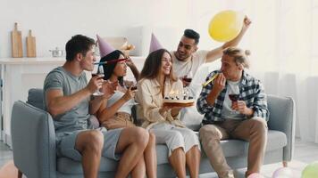 un grupo de diverso millennials disfruta un divertido fiesta a hogar, compartiendo la risa y bebidas mientras celebrando con un delicioso pastel y festivo decoraciones el atmósfera es animado y alegre. video