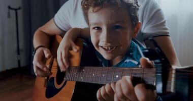 A young boy joyfully learns guitar from his father, showcasing love video