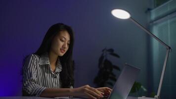 A woman using a laptop under a desk lamp video