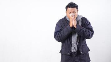 Unhealthy man wearing jacket and wool scarf blows his nose with tissue paper, suffering from flu isolated on white background photo