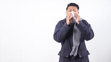 Unhealthy man wearing jacket is suffering from flu and sneezing using tissue paper isolated on white background photo