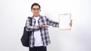 Smiling young Asian male college student with a backpack holding clipboard with blank paper mock up isolated on white background photo