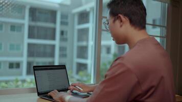 A man intently types on his laptop, his face illuminated by the screen, while the blurry cityscape outside hints at the bustling world beyond.Displays a web page with a text interface video
