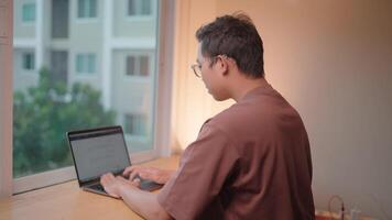 Focused Work A young man concentrates intently as he types on his laptop, eyes fixed on the screen. The natural light streaming through the window creates a calm and focused atmosphere. video