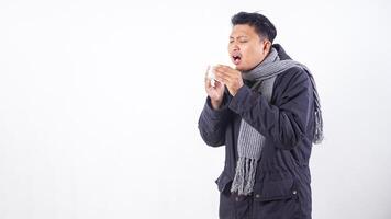 Portrait of unhealthy man wearing jacket is suffering from flu and sneezing using tissue paper isolated on white background photo