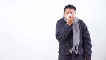 Portrait of sick man wearing jacket is suffering from flu and sneezing using tissue paper isolated on white background photo