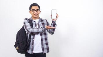 Portrait of cheerful young Asian male college student with a backpack showing blank screen of smartphone mock up isolated on white background photo