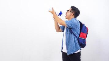 Side view of young Asian male university student in casual outfit with backpack is shouting on megaphone isolated on white background with copy space photo