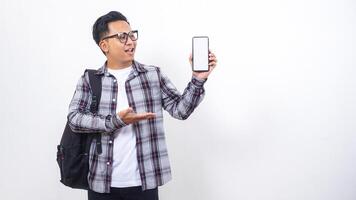 Portrait of young Asian male college student with a backpack showing blank screen of smartphone mock up isolated on white background photo