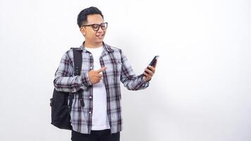 Excited young Asian male college student with a backpack holding smartphone isolated on white background photo