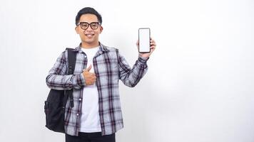 Portrait of smiling young Asian male college student with a backpack showing blank screen of smartphone mock up isolated on white background photo