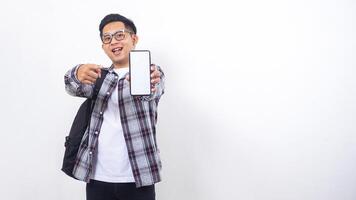 Excited young Asian male college student with a backpack showing blank screen of smartphone mock up isolated on white background photo