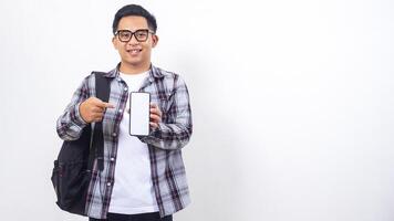 Handsome young Asian male college student with a backpack showing and pointing at blank screen of smartphone mock up isolated on white background photo