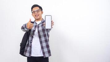 Cheerful young Asian male college student with a backpack showing blank screen of smartphone mock up isolated on white background photo
