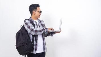 Side view of smiling young Asian male college student with a backpack and touching open laptop notebook isolated on white background photo