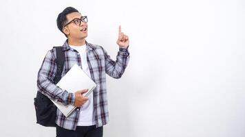Portrait of handsome young Asian male college student with a backpack and holding laptop netbook while showing gesture of number one isolated on white background photo