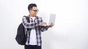 Portrait of smiling young Asian male college student with a backpack and touching open laptop notebook isolated on white background photo