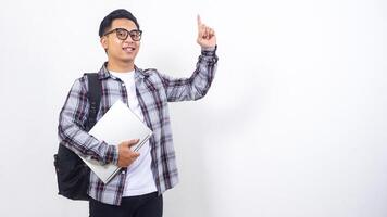 Handsome young Asian male college student with a backpack and holding laptop netbook while showing gesture of number one isolated on white background photo