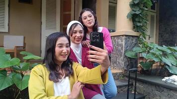 Three women are taking a selfie using a smartphone in front of a house. They look happy, there is luggage beside them, indicating a trip or vacation. video