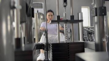 Portrait of a focused young woman engaged in strength training, utilizing a rowing machine at the gym for her physical fitness routine and wellness practice. video