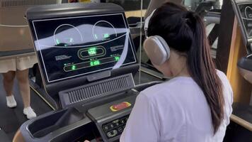 A woman wearing headphones uses a treadmill during a workout, monitoring her progress on the display. She is focused on achieving her fitness goals through dedicated exercise. video