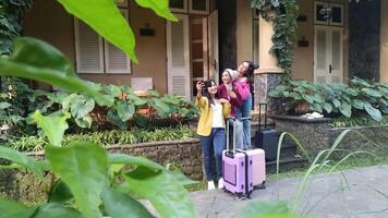 Three cheerful women are taking a selfie in front of a hotel during their vacation, luggage, and having fun together. They are enjoying their holiday. video