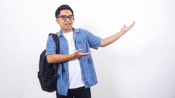 Portrait of smiling young Asian male university student in casual outfit with backpack is presenting empty space isolated on white background photo