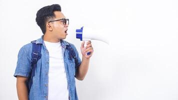 Portrait of excited young Asian male university student in casual outfit with backpack is shouting on megaphone isolated on white background photo
