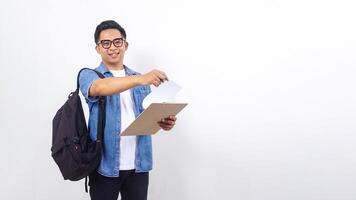 Smiling young Asian male university student in casual outfit with backpack and clipboard isolated on white background photo