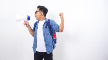 Side view of young Asian male university student in casual outfit with backpack is shouting on megaphone isolated on white background photo
