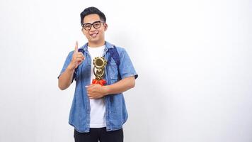 Handsome young Asian male university student in casual outfit with backpack is holding trophy isolated on white background with copy space photo