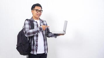 Happy young Asian male college student with a backpack and pointing his finger to open laptop notebook isolated on white background photo