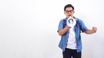 Portrait of unhappy young Asian male university student in casual outfit with backpack is shouting on megaphone isolated on white background with copy space photo