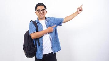 Portrait of happy young Asian male university student in casual outfit with backpack is presenting empty space isolated on white background photo