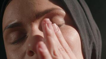 woman wearing hijab softly applies cream to face contemplative expression illuminated natural light creating peaceful and reflective atmosphere video