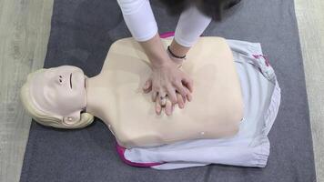 CPR training on a medical dummy with hands positioned correctly for chest compressions, a person in black sweatshirt demonstrates emergency response during a first aid course video