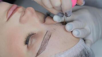 Permanent eyebrow tattooing in progress using hair-stroke technique, cosmetologist applies pigment with fine needle for natural brow effect on female client video